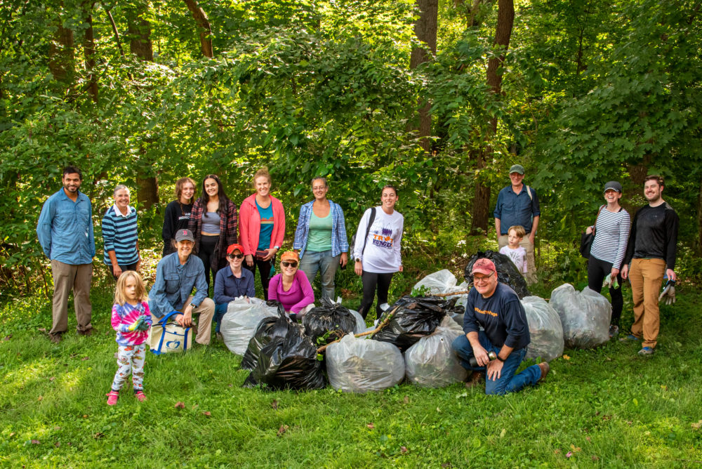Photo of a group of people and dozens of full trash bags in front of a wooded area. Volunteers and some of the dozens of bags of English ivy and other invasives they removed during an activity organized by Rock Creek Conservancy. © Frank Gallagher